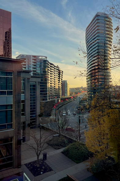 The image displays a photograph of a modern cityscape, likely taken during the golden hour. The style leans towards a realistic depiction with an emphasis on capturing the atmosphere and details of the scene.

The photograph emphasizes the geometric shapes and lines of the buildings, creating a sense of order and structure. The overall aesthetic is clean and contemporary, reflecting the modern architecture of the city. 