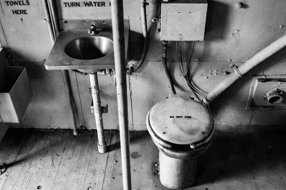 A black and white photo showing the very basic bathroom facilities inside an old bright red train caboose that's open to the public.