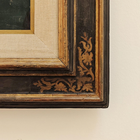 A close-up photo of the edge of an ornate wooden frame with gold detailing around the corner of a canvas with passe-partout 