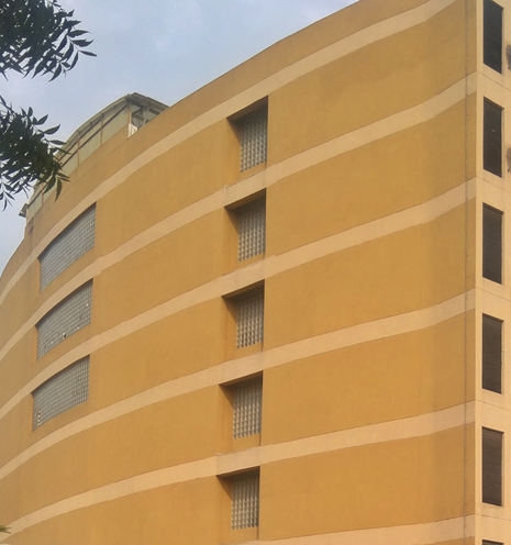 A beige building with horizontal lines and small rectangular windows, captured from below. A tree branch is visible in the upper left corner.
