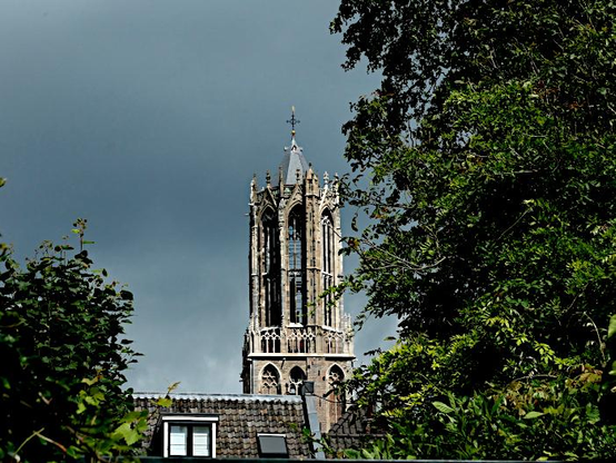 Foto van kerktoren achter huis en boom met donkere lucht