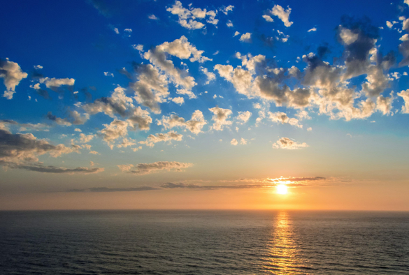 A photo of a sunset over the sea.

The bottom of the frame is entirely composed of sea, on a flattish, fairly calm day. The sun is just above the horizon, to the right of centre, and is reflected as a vertical orange stripe in the sea.

There is some scattered clouds, which is being illuminated from underneath, and on the horizon is a lovely band of orange light.