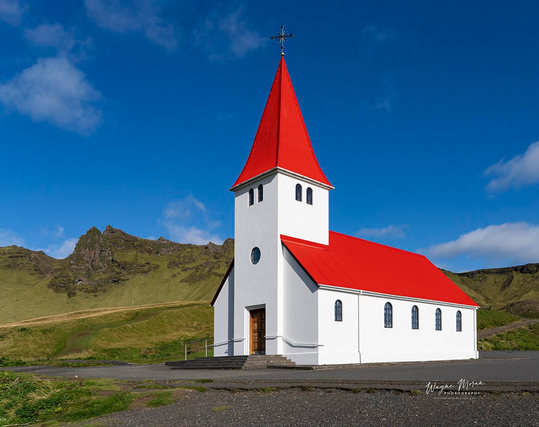 Vík í Mýrdal Church – Bright Morning Light Over Iceland’s Southern Coast

This photograph captures Vík í Mýrdal Church glowing in crisp morning light, its iconic red roof shining against a deep blue Icelandic sky. Set on a quiet hill above the village of Vík, the church stands clean and bright, surrounded by rolling green cliffs that rise dramatically behind it. The soft clouds drifting overhead and the calm, shadow free foreground create a peaceful and inviting scene.

Vík í Mýrdal Church is one of Iceland’s most beloved landmarks. Built in 1934, it overlooks the black sand beaches of the southern coast and serves as a symbol of hope and heritage for the community. Because it sits high above sea level, the church is also the town’s designated safe refuge during possible eruptions from nearby Katla, one of Iceland’s most powerful volcanoes. This gives the church a deeper significance, representing both beauty and protection in a rugged volcanic landscape.

In this composition, the brilliant red roof contrasts beautifully with the natural greens and blues of the surrounding mountains and sky. 

Image:
https://fineartamerica.com/featured/vik-i-myrdal-church-bright-morning-light-over-icelands-southern-coast-wayne-moran.html

Read more:
https://waynemoranphotography.com/blog/chasing-light-across-iceland-our-21-day-adventure/

#Church #architecture #Vik #landscape #Iceland #nature #travelPHotogrpahy #Landscape #art #fineart 

#ayearforart #buyintoart