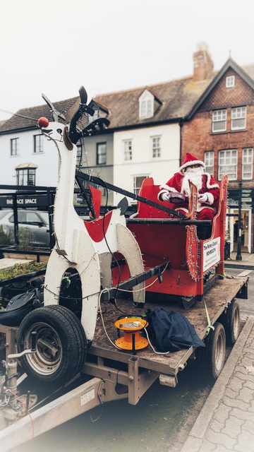 A Rotary Club Christmas float from Monmouth, featuring Father Christmas in a sleigh and a large wooden reindeer, parked on Monnow street ready to give out gifts, have photographs taken, and accept donations.