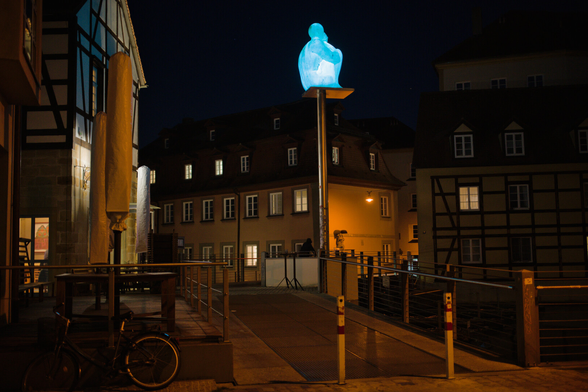 Innenstadt, Brücke übern Fluss, Alte Häuser zum Teil Fachwerl. Dunkel Beleuchtung. Eine Kunstfigur Leuchtet auf einem Pfal.