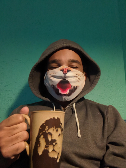 Black man wearing a hoodie and a cat mask with an open mouth holding a mug of coffee