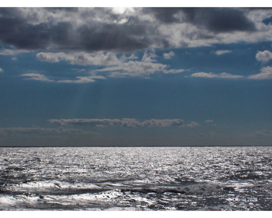 Bright sun rays peek through a cloudy sky over a shimmering ocean, creating a serene and reflective mood with a subtle, calm horizon.