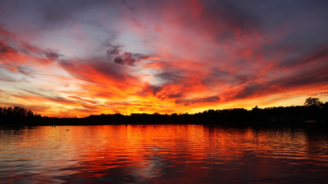 Sunset photo of bright yellow, orange, and pink clouds over a reflective lake.