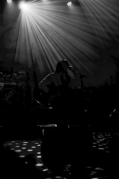 Photo noir et blanc d’une musicienne en contre-jour avec des rayons de lumières qui lui tombent dessus depuis un spot en haut de l’image et qui forment des cercles lumineux sur la scène