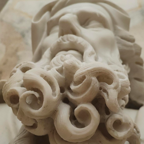 Fragment of a white marble sculpture with a highly detailed, stylized beard of the figure, which consists of large, deeply carved, spiral, and curl-like locks.