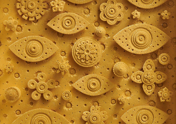 A textured yellow paper relief artwork featuring intricate circular patterns and shapes resembling eyes, flowers, and organic forms.