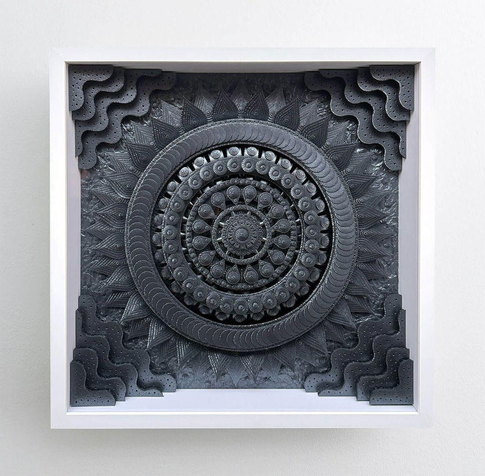 Intricate black and gray circular paper sculpture design with layered patterns and textures, framed in white, resembling a decorative mandala.