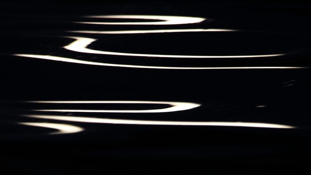 Photograph of white horizontal swoops on a black background created by moonlight reflected on the surface of a lake.
