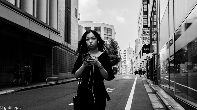 Noia amb auriculars i amb el mòbil a les mans, caminant pels carrers de Shinjuku.