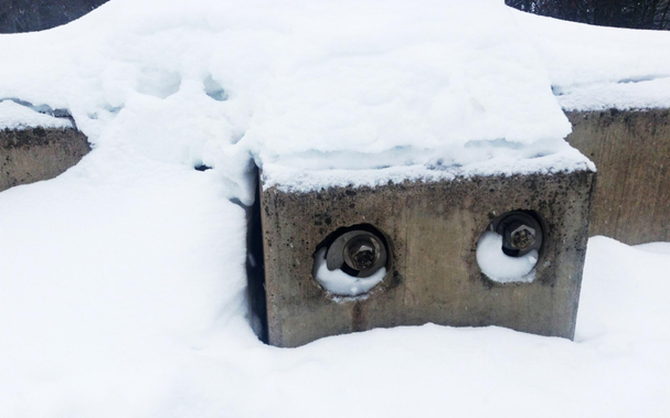 Snow-covered vertical concrete support member of a garage with two bolt holes filled with snow in such a way as to suggest rolling eyes.