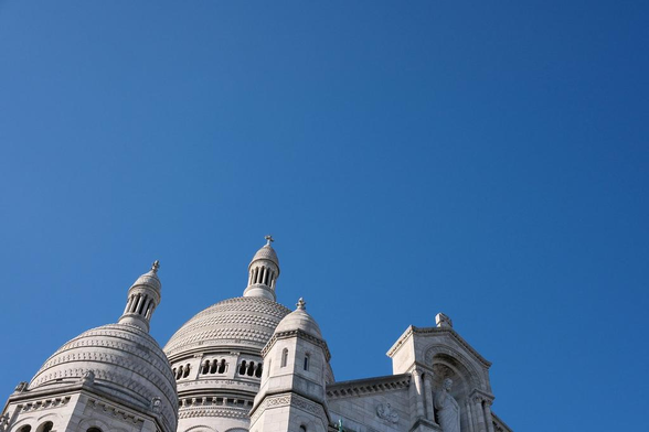Photo avec le haut du Sacré Cœur occupant 25% de l’image, le reste étant un ciel bleu parfait, contrastant avec la blancheur des pierres