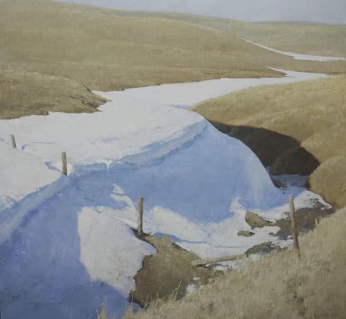 A serene landscape featuring snowbanks and gently rolling hills. The foreground shows a snowy area with a stream visible, bordered by wooden posts. The background consists of grassy hills under a light blue sky, suggesting early spring.