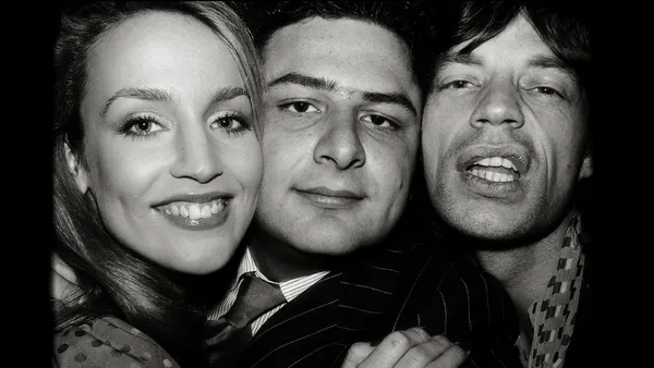 A black and white close-up of the faces of Jerry Hall, Johnny Pigozzi and Mick Jagger, close together.