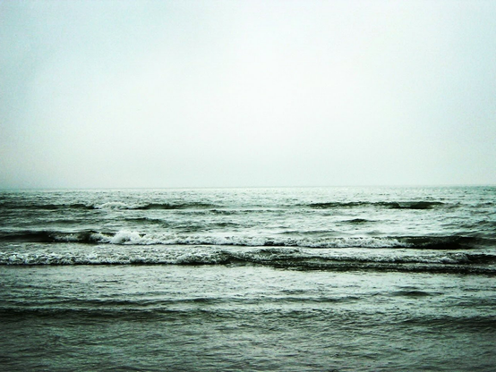 A black and white photo showing a view of an ocean with small waves and a white mist in the horizon.