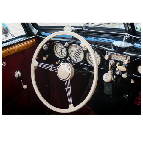 Blick in den Innenraum eines Oldimers. Lenkrad und Instrumente sind weiß. Das Dashboard ist schwarz.