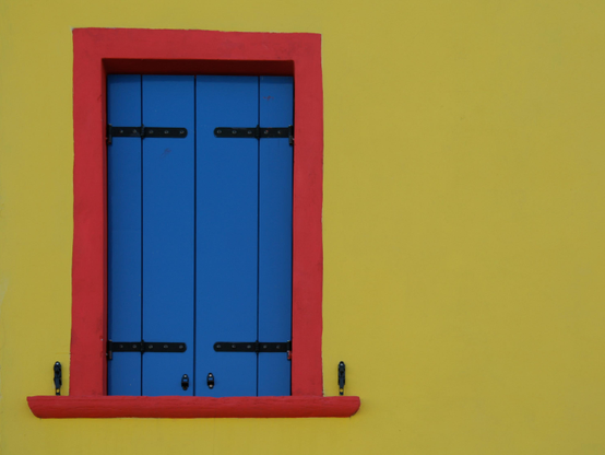 A blue window with red frame on a yellow wall.