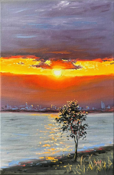 A striking landscape near a shore with one small tree in the foreground slightly to the right, with a patch of grasses nearby. In the middle distance on the further shore is a city. The sky is dominated by two big banks of clouds with a clear stripe in the middle where a golden sun sits with a small drifting cloud seeming to crown it. The upper layer of cloud is tinted greyish-blues with touches of white, the lower layer is an orange-red, the middle clear part is a deep golden yellow. The city, water, tree, and grasses are all touched with that light.