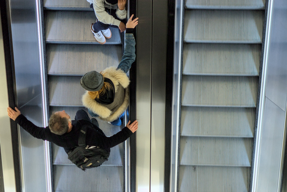 A man, woman and child on an escalator, viewed from above. The child is sitting down.