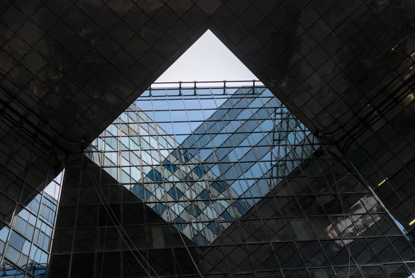 A shot of a glass office building through a square hole. The glass panes reflect against each other, forming a pyramid shape
