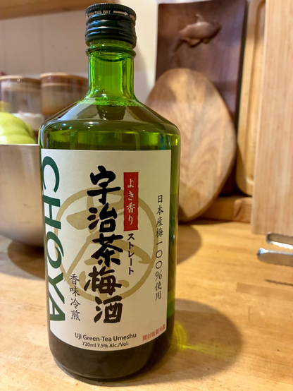 A green bottle of umeshu (Japanese plum wine) featuring a label with Japanese and Chinese characters indicating that it is plum wine infused with Uji green tea