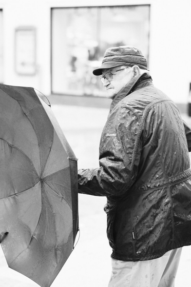 Das Foto zeigt eine Straßenszene in Schwarz-Weiß in der St. Pöltenter Innenstadt an einen regnerischen windigen Tag. Man sieht eine Person mit Regenschirm der durch den Wind verbogen ist.