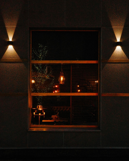 Late evening. In the close-up photo, the window of the cafe is illuminated by the warm light of indoor and outdoor lamps. The window shows a reflection of a tree decorated with garlands.