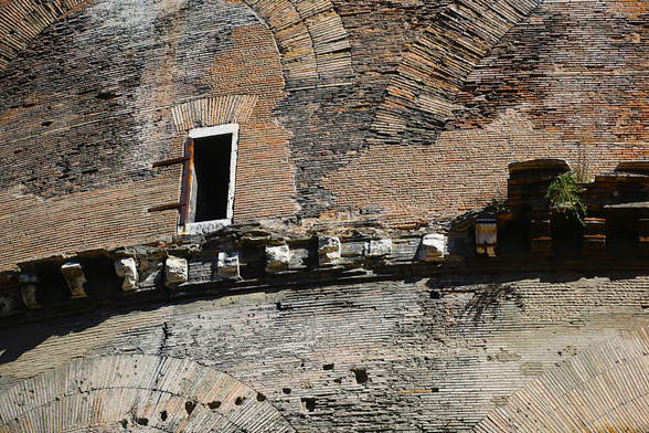 An ancient and battered, curved wall, which is made from red bricks. There is a band of broken, marble protuberances part-way up, and a small, rectangular, window opening just above the marble band.
