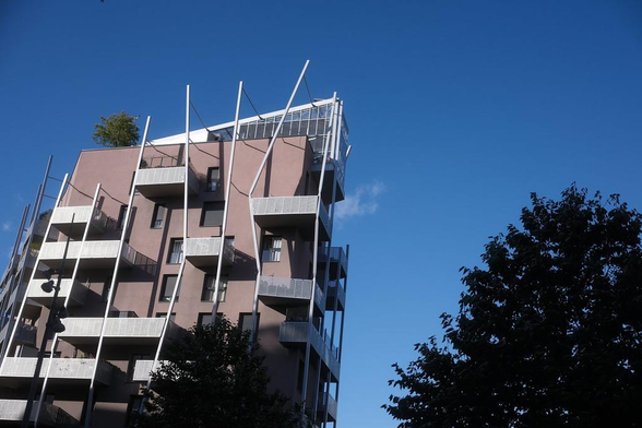 Photo couleur d’un immeuble à l’architecture futuriste, en forme de trapèze, sur fond de ciel bleu et un arbre à droite de l’image