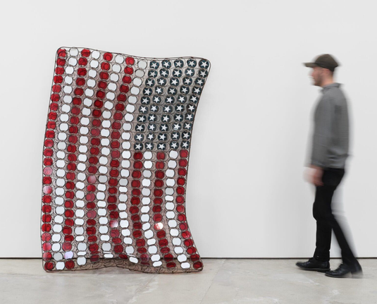 a man walking up to a large metal american flag on its side