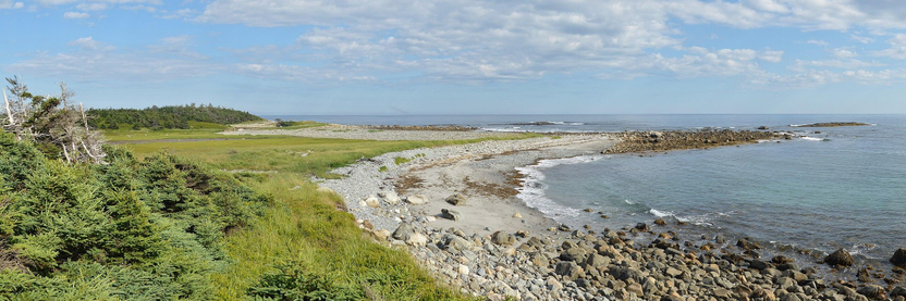 A panoramic photo of a rocky coast. The sky is blue with some white clouds in it.