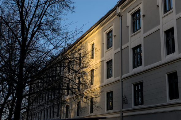 An apartment building is in the shade. The sun is coming up late in the Scandinavian winter, and the first rays of light are hitting the middle of the building only, while the rest is still in darkness.