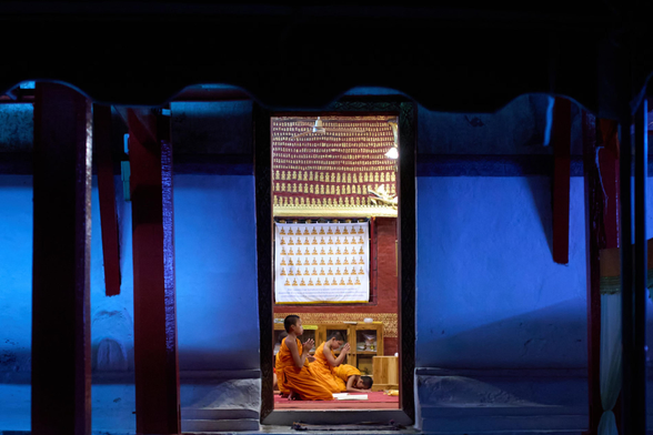 Novice Buddhist monks pray in a temple as the evening light fades outside.