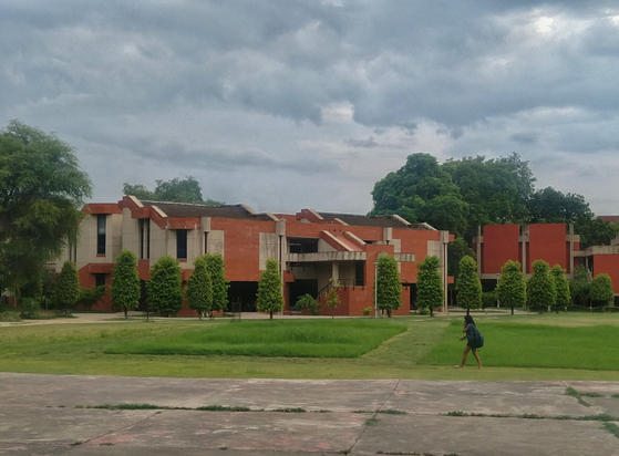 Modern brick and concrete building amid lush greenery under a cloudy sky. A student walks on a pathway.