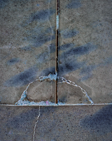 A section of concrete walkway divided into areas by expansion gaps and stress cracks. A very formal and minimal composition.