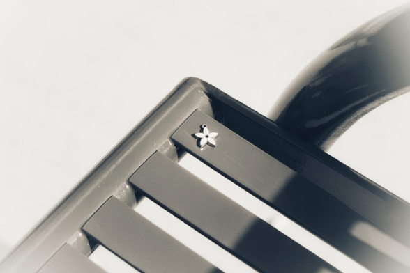 A small star shaped pendant sits on the corner of a metal bench. Only the corner of the bench is seen and the background is pure white in this black and white image.