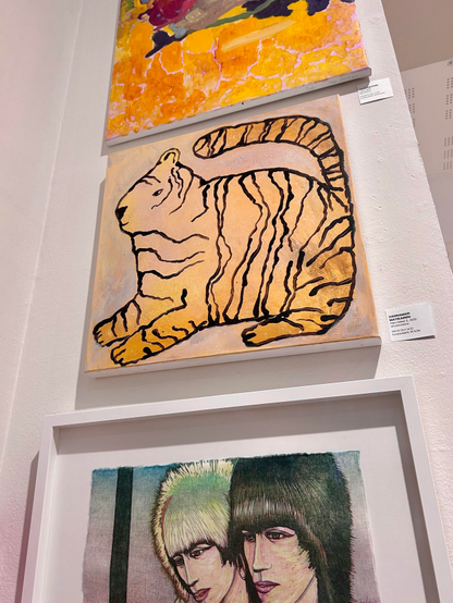 На выяве прадстаўлены тры творы мастацтва, размешчаныя на сцяне. Верхні твор — абстрактная карціна з яркімі колерамі, пераважна жоўтым. Сярэдні твор адлюстроўвае стылізаваную, контурную выяву тыгра ў аранжавых і чорных танах.