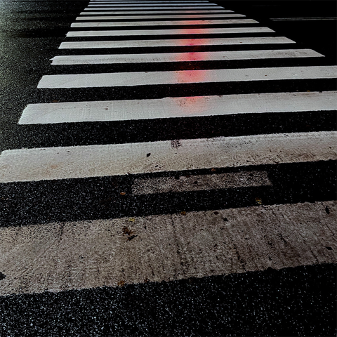 A wet crosswalk at night, featuring bold white stripes on dark asphalt, illuminated by a faint red glow.