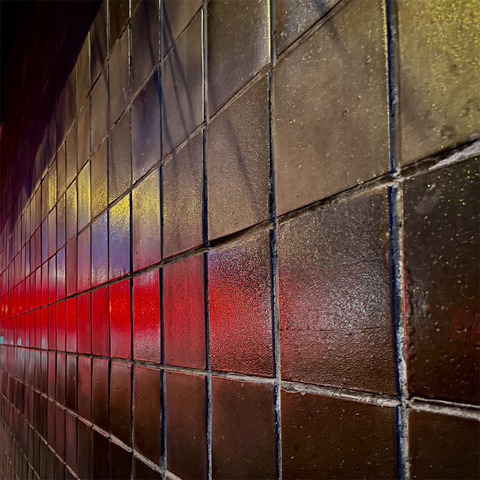 A close-up view of dark, glistening tiles reflecting vibrant red and yellow lights, creating an abstract, textured wall appearance.