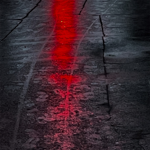A glistening, dark pavement reflects a bright red light, creating a striking contrast against the wet surface.