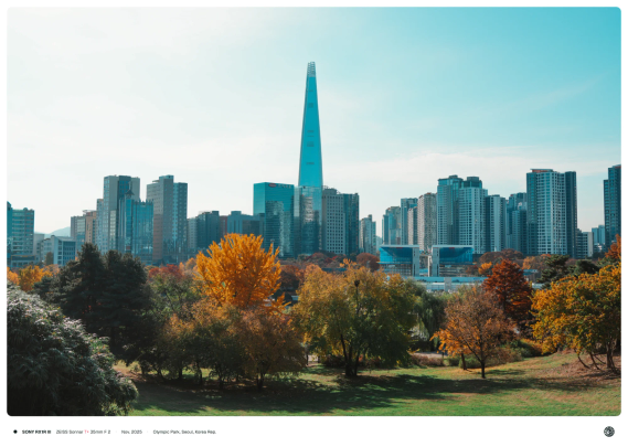 단풍이 진 나무가 무성한 올림픽 공원과 평화의 문 뒤로 무수한 빌딩이, 그 뒤로는 롯데월드타워가 한가운데 우뚝 서 있는 모습.