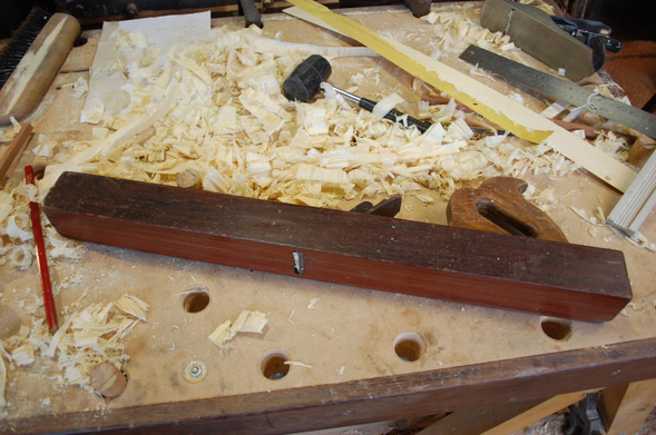 Dite la locomotive, tellement lourde que quand elle est lancée, elle ne s’arrête plus. Elle fait environ 80 cm de long, en bois précieux, fabriquée par mon grand-père. Je ne l'utilise plus en ce moment car il faut que je lui reprenne la lumière, qui est devenue trop grande à force de surfaçage de la semelle.
Elle est posée sur mon premier établit (voir un post précédent) avec plein de copeaux, un maillet avec une tête en caoutchouc, une équerre de charpentier, un rabot n°5 classique, un crayon de charpentier rouge.