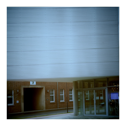 Silbrige queergestreifte Hauswand, darunter und weiter hinten ein Wand aus Backstein mit Durchgang