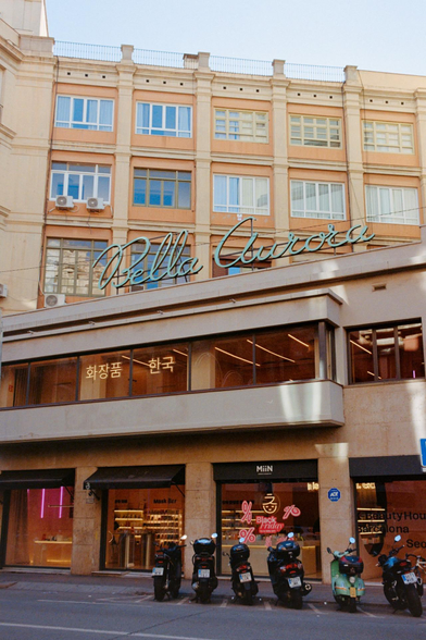 Fotografía del número 5 de Calle Balmes en Barcelona. En la imagen se ve un edificio con el rótulo "Bella Aurora", varias motos delante y la luz del atardecer asomando por el lateral.

Photograph of 5 Balmes Street, Barcelona. The image shows a building with the sign "Bella Aurora" (beautiful Aurora), several motorcycles in front and the light of the setting sun peeking in from the side.