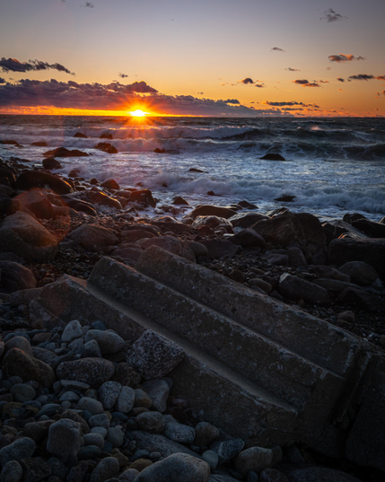 A photograph of sunset over the water at Gooseberry Island. One of the concrete stairways from the cabins that used to be on the island is in the foreground. 
