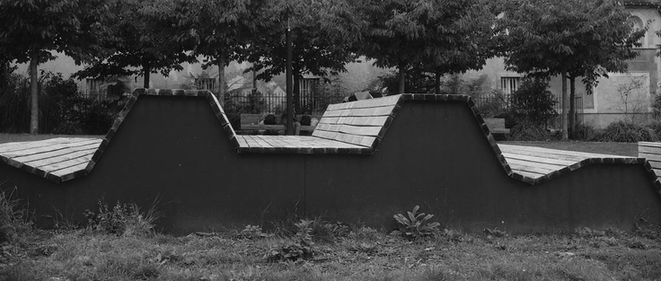 Photo noir & blanc d’un mobilier urbain, des bancs, en bois mais avec une forme singulière, de profil on dirait une courbe de signal électrique